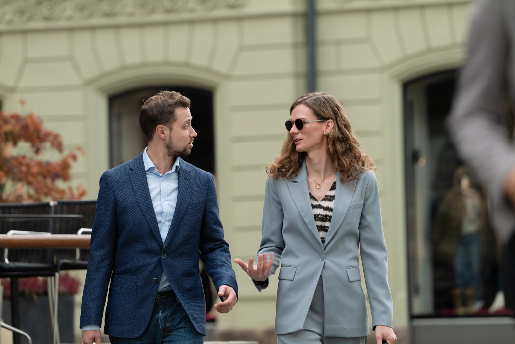 Une femme portant des lunettes de soleil avec des verres de première qualité de Leica se promène dans le centre-ville en compagnie d'un homme et échange avec lui.