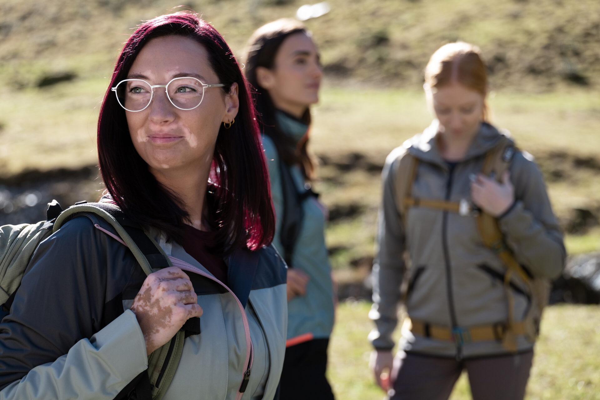 Junge Frau mit Brille mit Premium-Brillengläsern von Leica wandert mit zwei Freundinnen in den Bergen