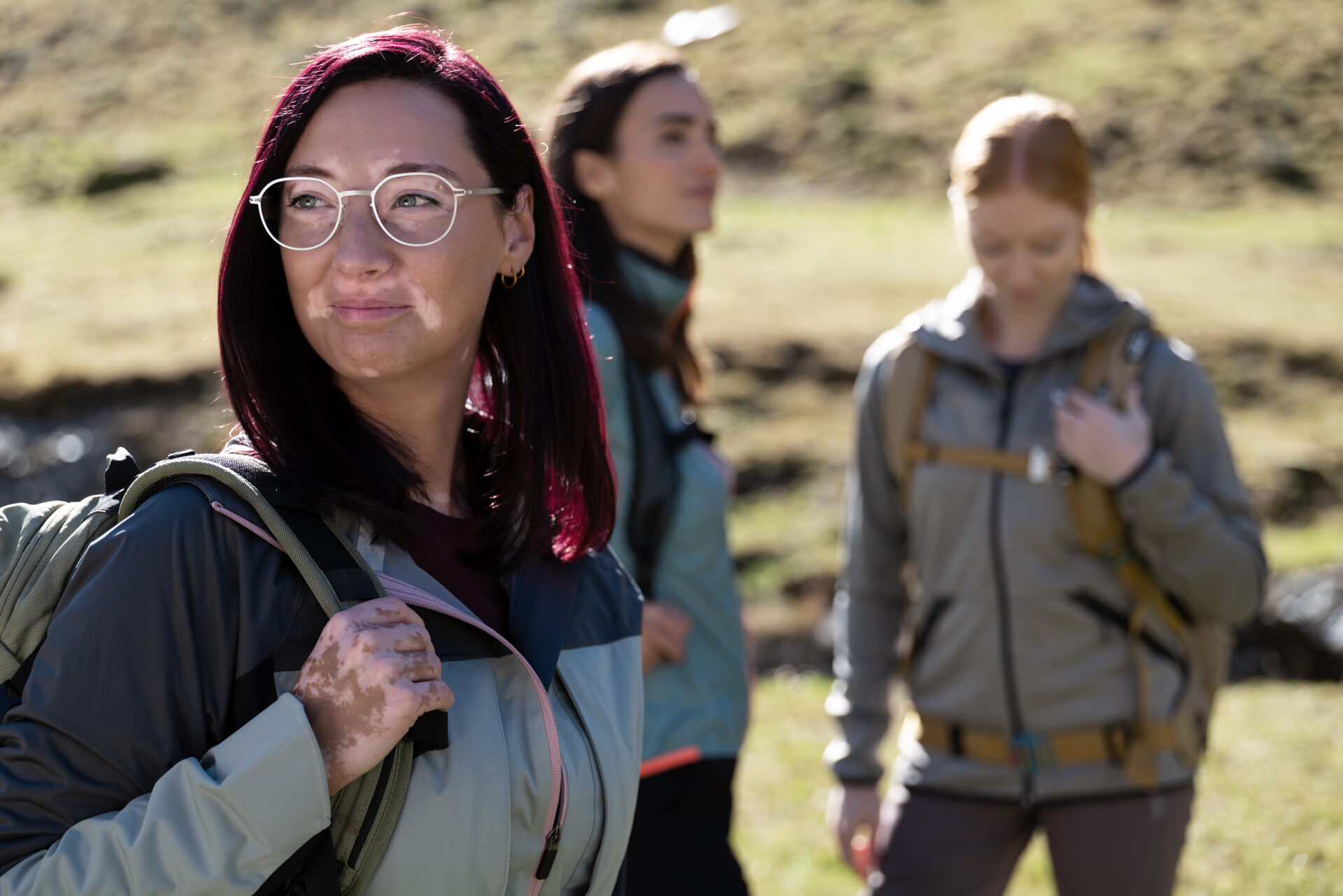 Une jeune femme portant des lunettes avec des verres de première qualité de Leica fait une randonnée en montagne avec deux amies